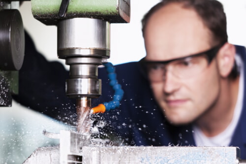 worker drilling a hole in a piece of metal using safety glasses