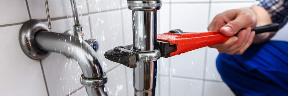Plumber using a pipe wrench to loosen pipes on a sink